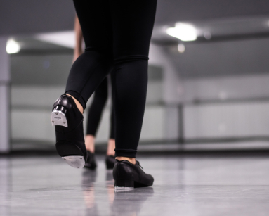 Close-up of dancers wearing black tap shoes and leggings practicing in a dance studio.